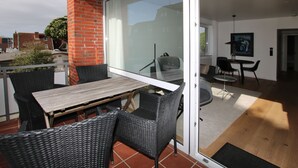 Ein Balkon mit Korbmöbeln, einem Holztisch und einer Glastür zu einem Essbereich im Innenbereich mit einem runden Tisch und Stühlen.