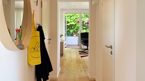Ein Flur mit Holzboden, einem Spiegel, einer gelben Tasche und einer Tür, die auf einen Balkon mit Blick ins Grüne führt.