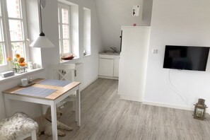 A modern kitchen with white cabinets, a dining table with a placemat, and a TV mounted on the wall. - Ferienwohnung mit 2- Zimmern auf ca. 30m², Hyggelig (Wyk auf Föhr)