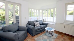 Ein helles Zimmer mit zwei grauen Sofas, einem kleinen runden Tisch und einem Fenster mit Blick auf Grünflächen.