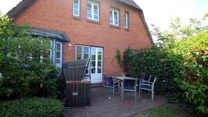 Ein Backsteinhaus mit einem Strohdach, eine Terrasse mit Tisch und Stühlen sowie ein kleiner Garten.