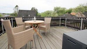 Eine Holzterrasse mit Korbmöbeln und einem Grill.