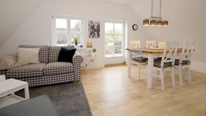 Ein gemütliches Wohnzimmer mit einem karierten Sofa, einem Esstisch mit Stühlen und einem kleinen Beistelltisch mit einer Lampe.