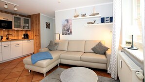 A modern living room with a beige sofa, a coffee table, and a kitchen area with wooden cabinets and a microwave.