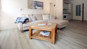 Un salon avec un canapé beige, une table basse en bois et une cuisine en arrière-plan.