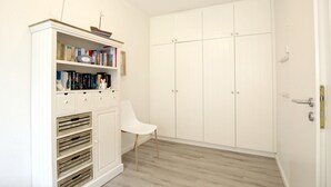 Une pièce avec une armoire blanche, une chaise blanche et une bibliothèque.