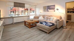Un salon moderne avec un canapé beige, une table basse en bois et une vue sur le paysage urbain, visible à travers de grandes fenêtres.