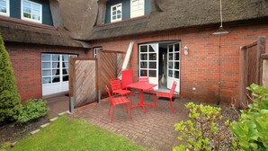 Una casa de ladrillo con techo de paja, un portón de madera y un patio con mobiliario rojo.