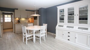 Una cocina moderna con armarios blancos, una mesa de comedor con sillas y un mueble empotrado con puertas de vidrio.