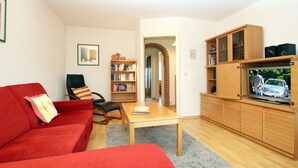 Una sala de estar con un sofá rojo, una mesa de centro de madera, una estantería y un mueble para televisión con un televisor.