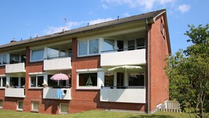 Un edificio de apartamentos de ladrillo con dos pisos, balcones, un pequeño jardín y cielo despejado.