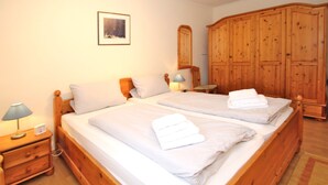 Una cama doble con sábanas y toallas blancas, una mesita de noche de madera con lámpara, un armario de madera y un cuadro en la pared.