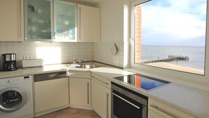 Eine Küche mit Waschmaschine, Geschirrspüler, Herd und Meerblick durch ein Fenster.