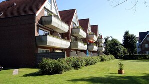 Uma fileira de edifícios de apartamentos modernos com varandas, um gramado bem cuidado e um céu limpo.