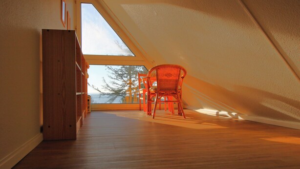 Um quarto no sótão com piso de madeira, uma cadeira vermelha e um amplo claraboia.