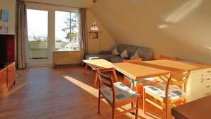 Uma área de refeições com mesa e cadeiras de madeira, um sofá e vista para o exterior por uma porta de correr.