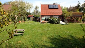 Een huis met een rode dakbedekking van tegels, een zonnepaneel, een gazon, een schommel en een bank.
