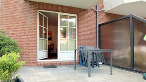 Un'area patio con tavolo e sedie, una porta scorrevole in vetro che dà su una stanza e un muro in mattoni.