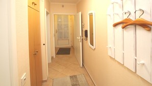 Un corridoio con una porta in legno, un appendiabiti bianco a parete e un campanello.