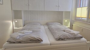 Un letto matrimoniale con biancheria e cuscini bianchi, due comodini con lampade e una finestra con tende.