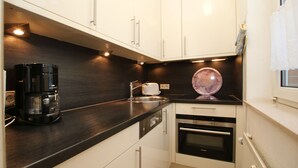 A compact kitchen with white cabinets, a black countertop, a coffee maker, a toaster, and a built-in oven. - Ferienwohnung mit 2-zimmern mit ca. 45m² und Balkon (Wyk auf Föhr)