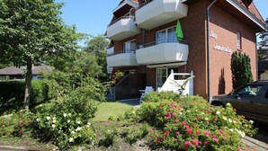 A two-story building with a brick facade, multiple balconies, and a garden with various plants and flowers. - Ferienwohnung mit 2-zimmern mit ca. 45m² und Balkon (Wyk auf Föhr)