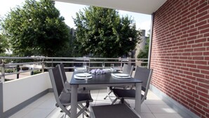 A balcony with a table set for four, surrounded by chairs, and a brick wall to the right. - Ferienwohnung in Wyk/ Südstrand mit ca. 56m² und 3- Zimmern in der Ersten Etage (Wyk auf Föhr)