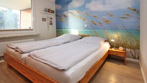 A bedroom with a wooden bed, a nightstand, and a beach mural on the wall. - Ferienwohnung in Wyk/ Südstrand mit ca. 56m² und 3- Zimmern in der Ersten Etage (Wyk auf Föhr)