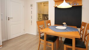 A dining area with a wooden table, four chairs, and a pendant light. - Ferienwohnung in Wyk/ Südstrand mit ca. 56m² und 3- Zimmern in der Ersten Etage (Wyk auf Föhr)