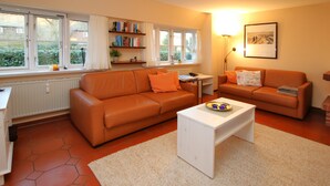 A living room with two orange sofas, a white coffee table, and a bookshelf. - Ferienwohnung in Wrixum, mit 2- Zimmern auf 51m² im Reetdachhaus (Wrixum)