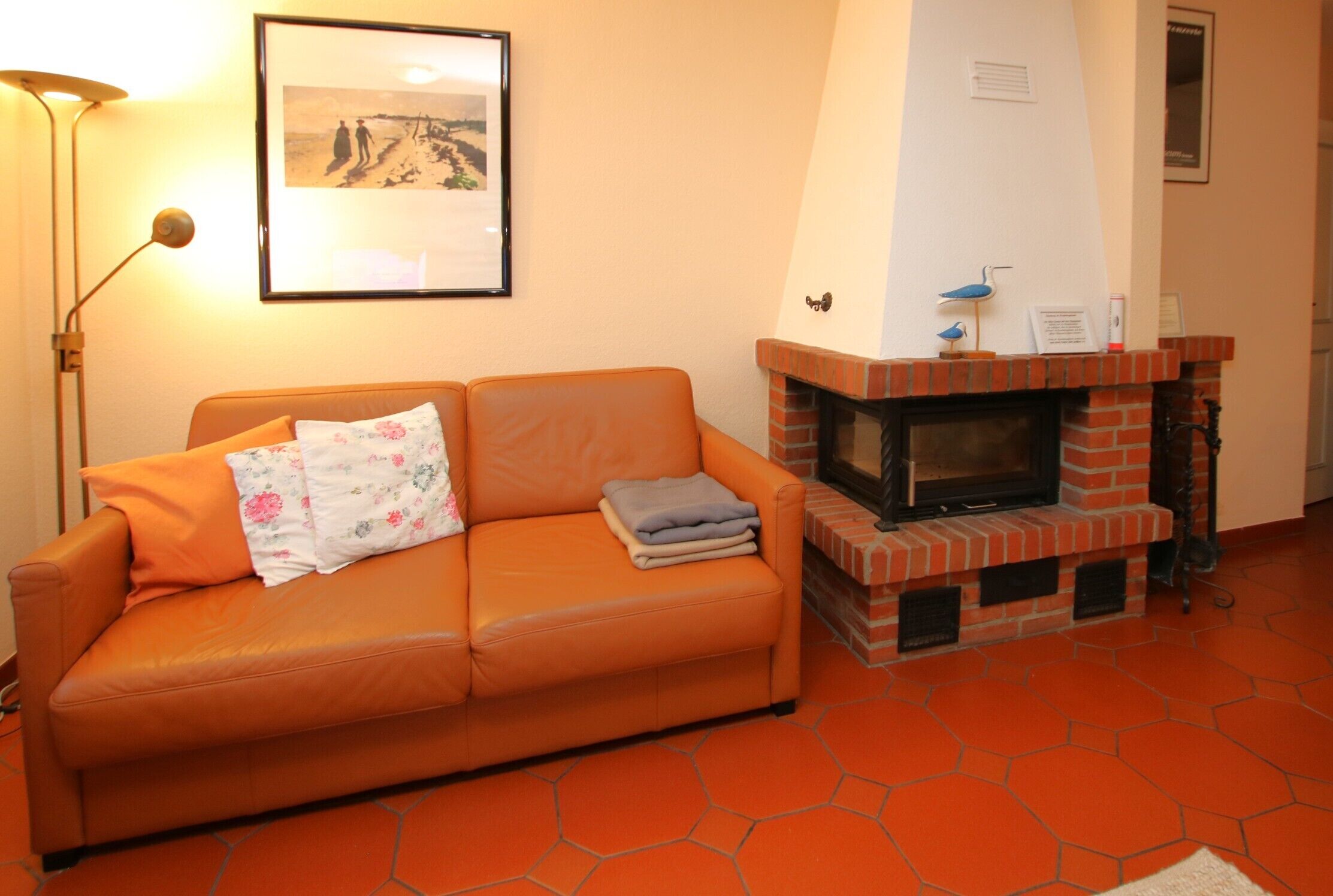 A room with a brick fireplace, orange sofa, and a framed picture on the wall.