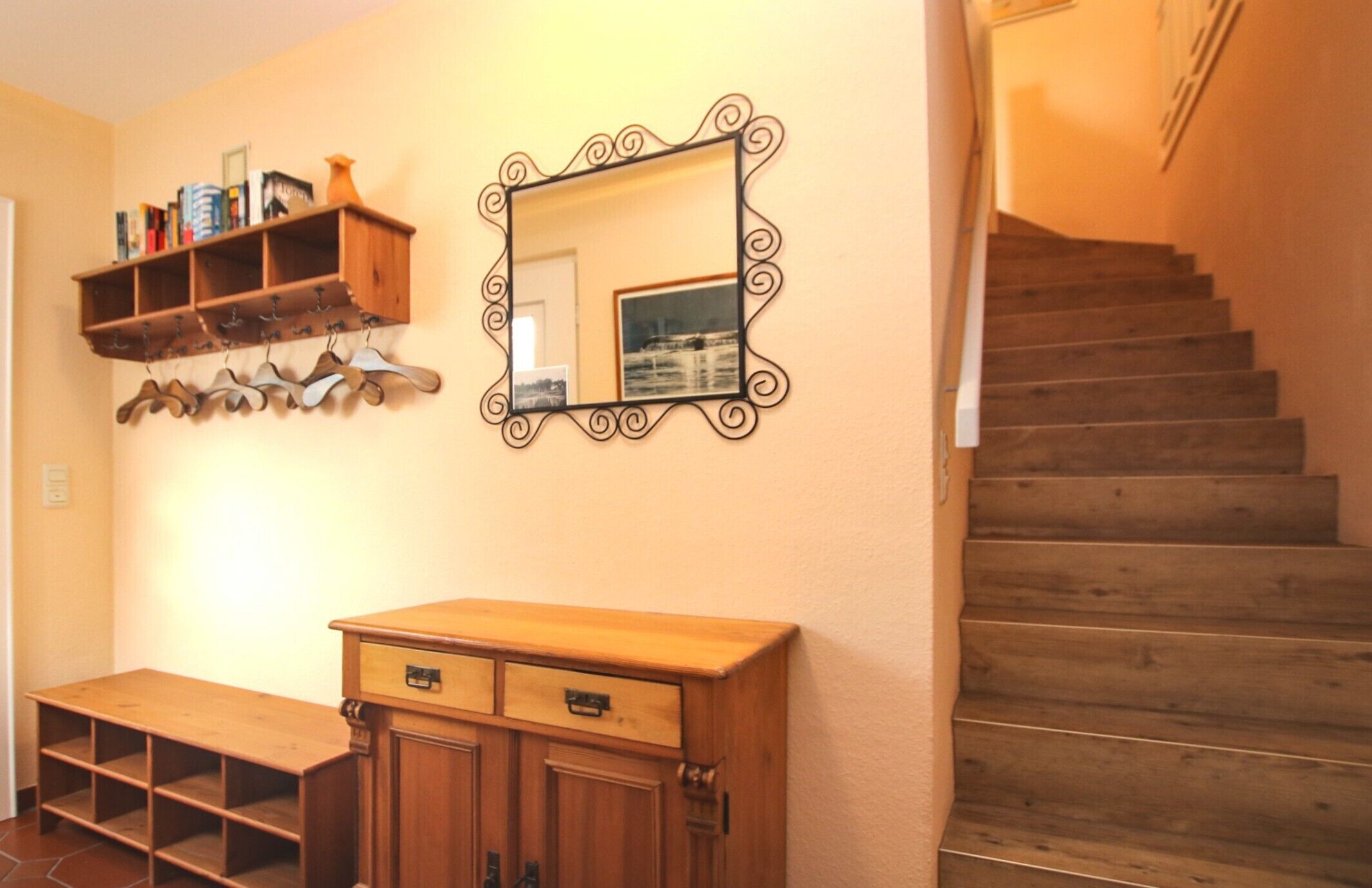 A wooden bench, a mirror, a wooden shelf with books, and a staircase.