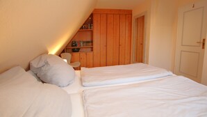 A bedroom with two beds, a wooden bookshelf, and a door. - Ferienwohnung in Wrixum, mit 2- Zimmern auf 51m² im Reetdachhaus (Wrixum)