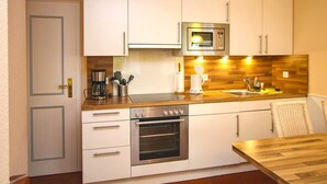A compact kitchen with white cabinets, a built-in microwave, a coffee maker, and a sink. - Ferienwohnung in Wrixum, mit 2- Zimmern auf 51m² im Reetdachhaus (Wrixum)