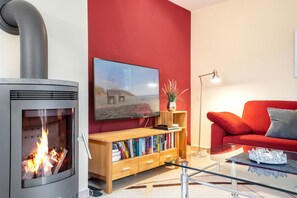 Un salon avec une cheminée, un mur rouge, un canapé, une table basse et une bibliothèque.