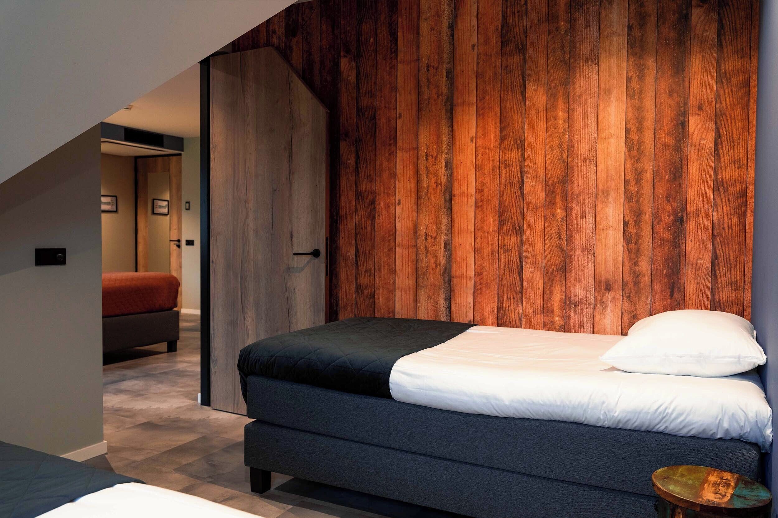 Une chambre moderne avec un mur d’accent en bois, un lit avec une literie aux couleurs sombres et une petite table ronde.