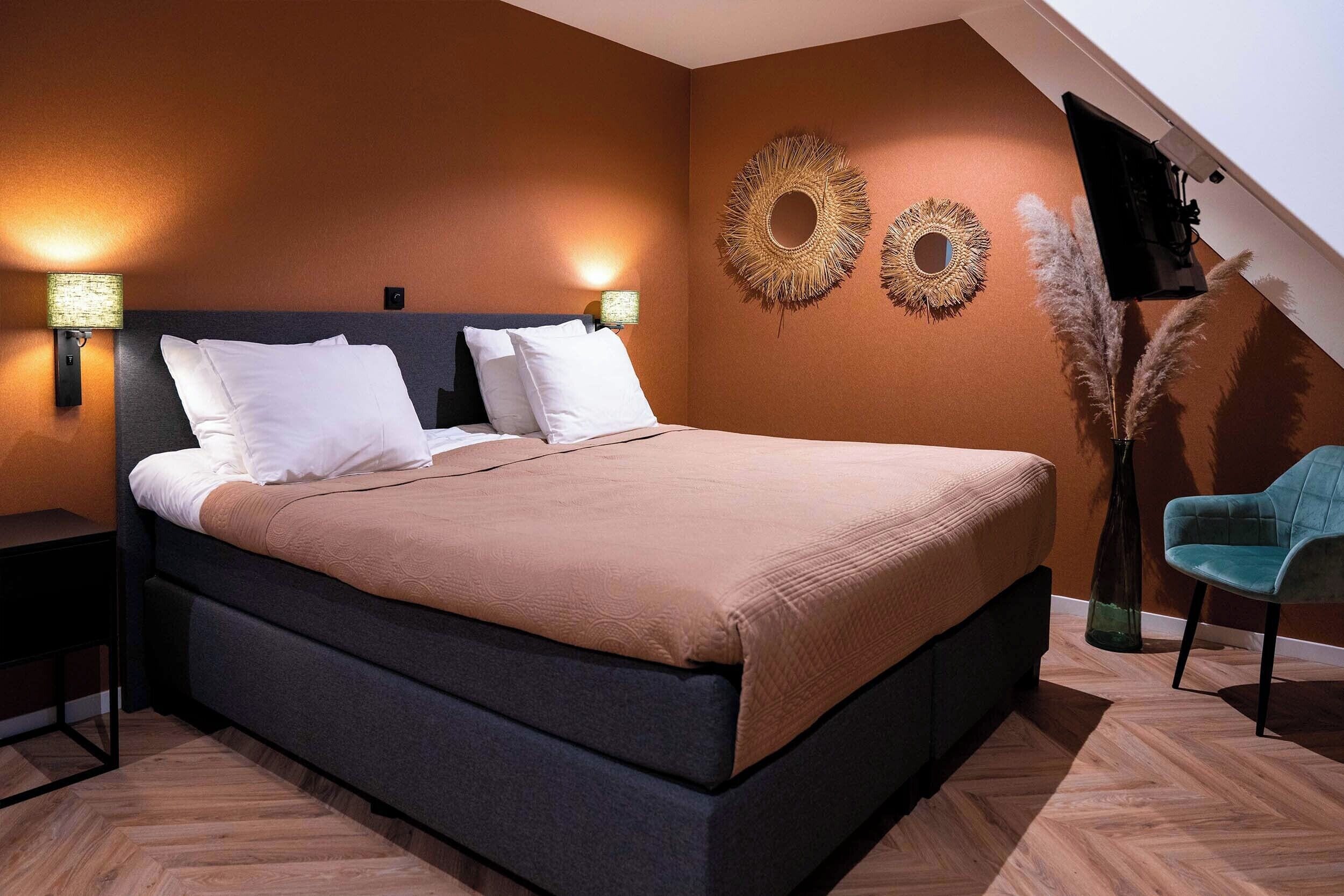 A bedroom with a bed, two wall sconces, decorative wall art, a chair, and a TV mounted on the wall.