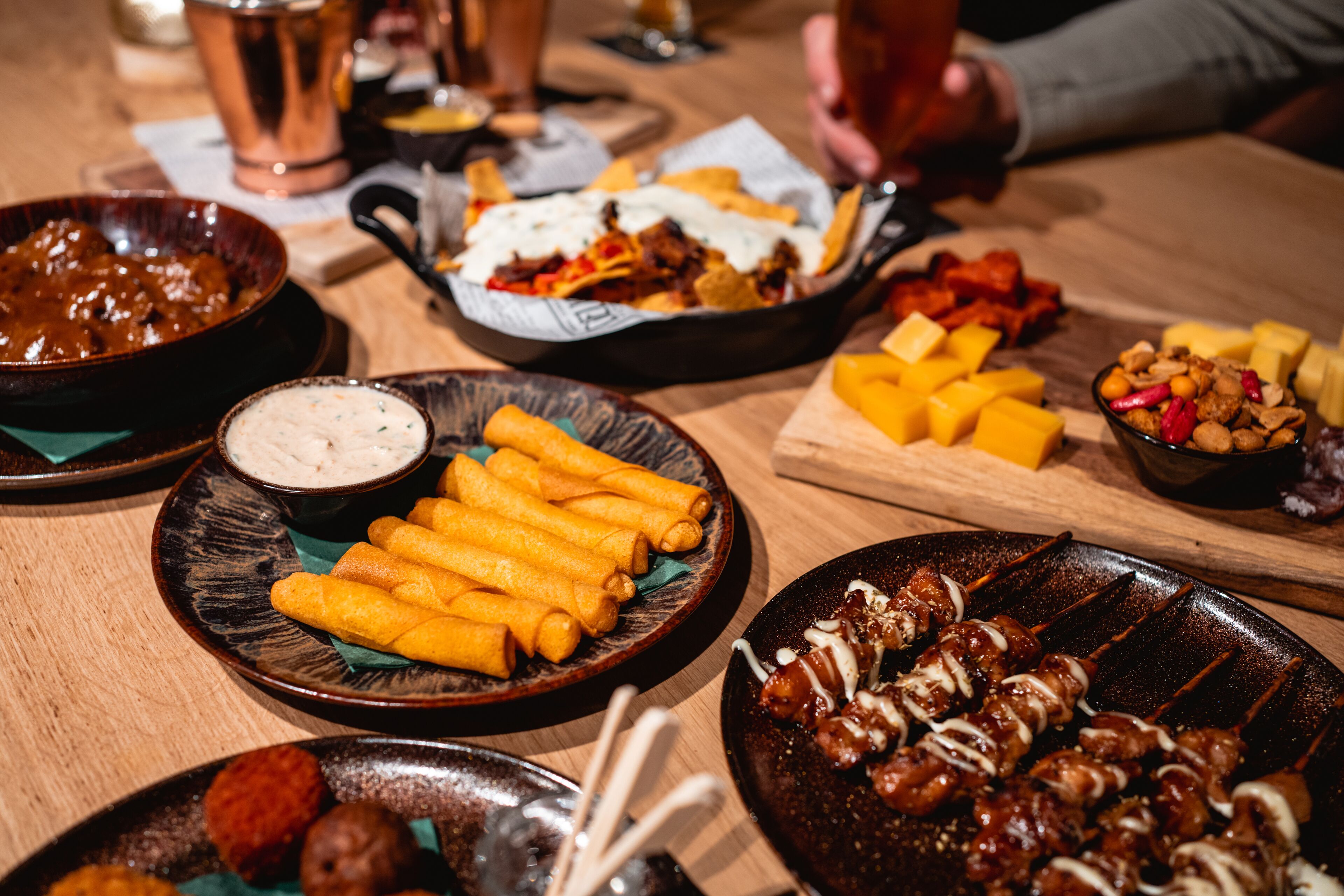 A variety of dishes including fried items, skewers, and a bowl of dipping sauce on a wooden table.