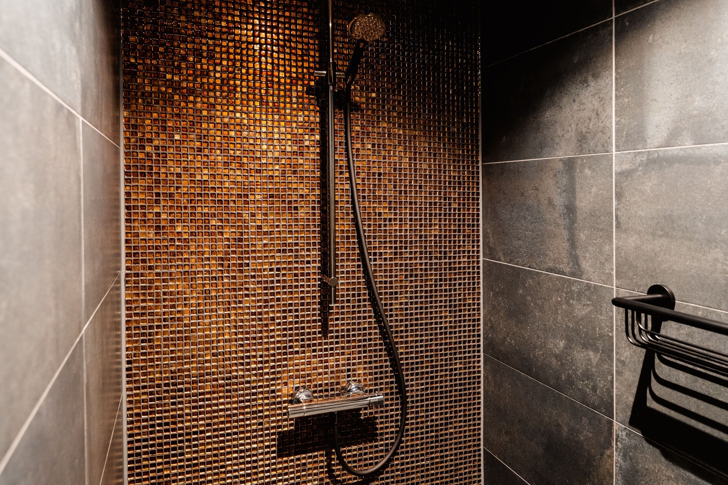 A shower with a mosaic tile wall, a handheld showerhead, and a towel rack.