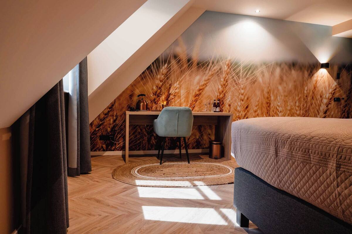Une chambre avec un plafond en pente, un lit, un bureau avec une chaise et un mur orné de hautes herbes.