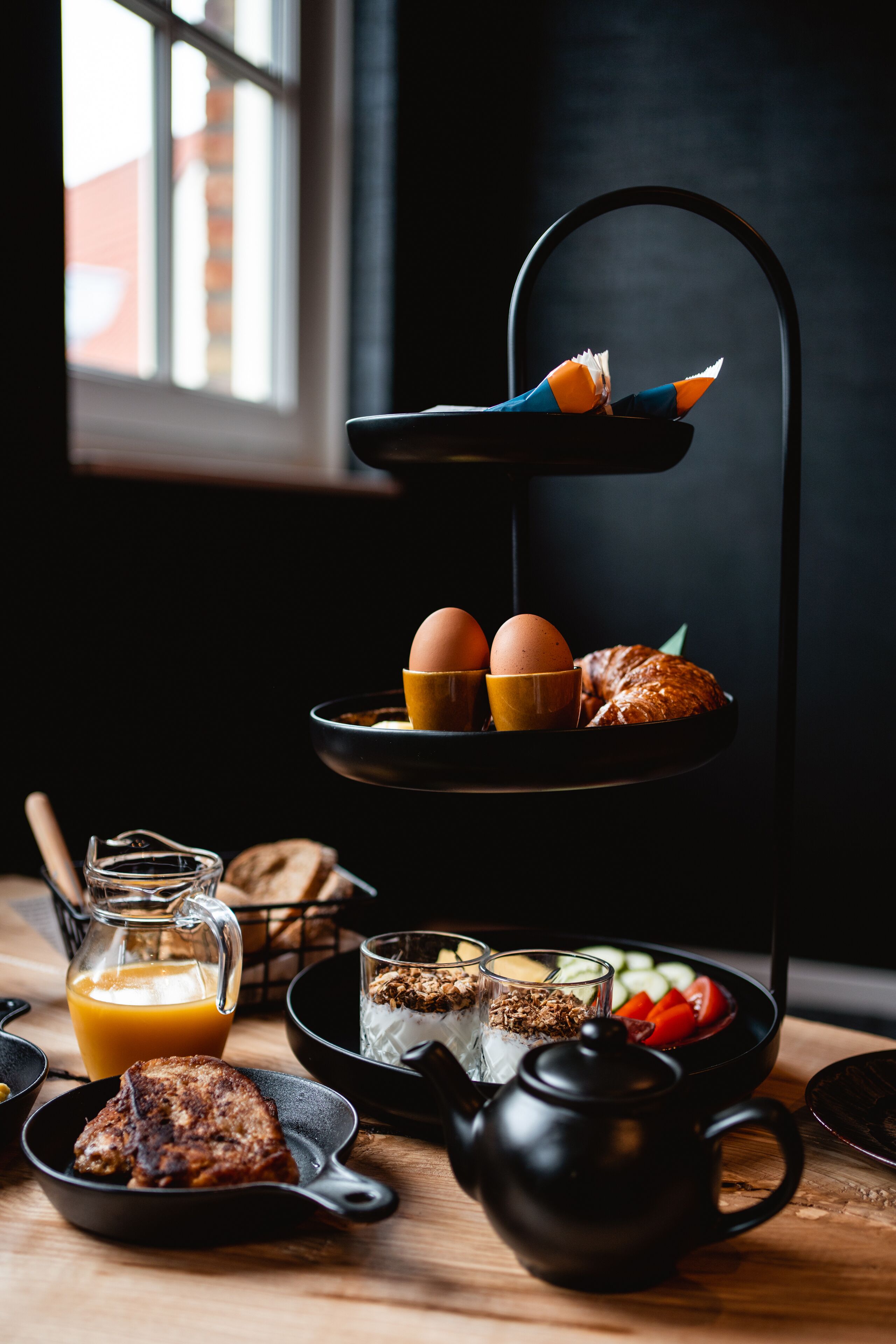 A breakfast setup with eggs, croissants, and a teapot on a tiered stand.