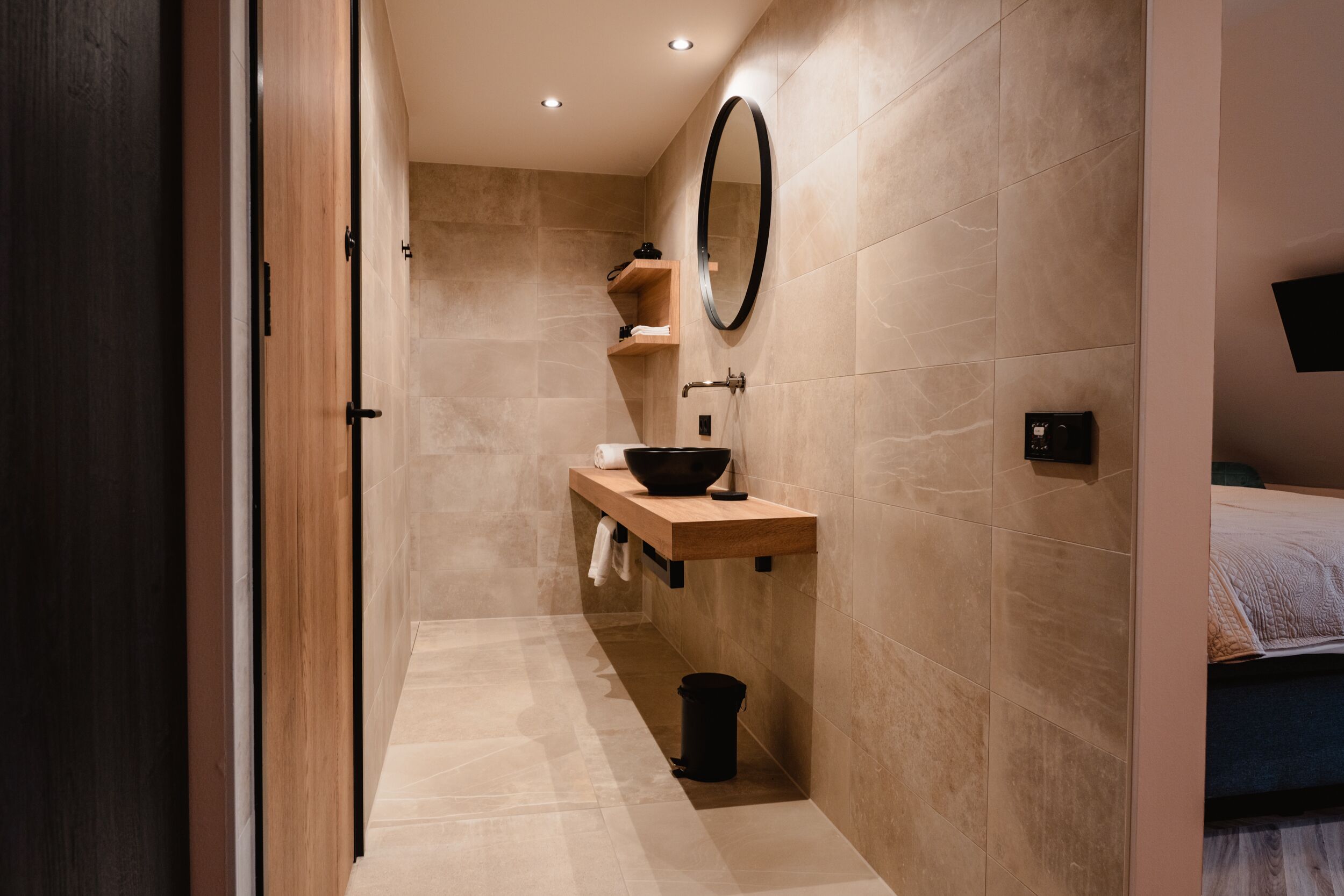 A modern bathroom with a wooden vanity, a black sink, a mirror, and a shower area.