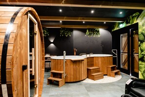A wooden sauna with a large tub, wooden steps, and a black wall with green plants. - Othmar Herberg (Ootmarsum)
