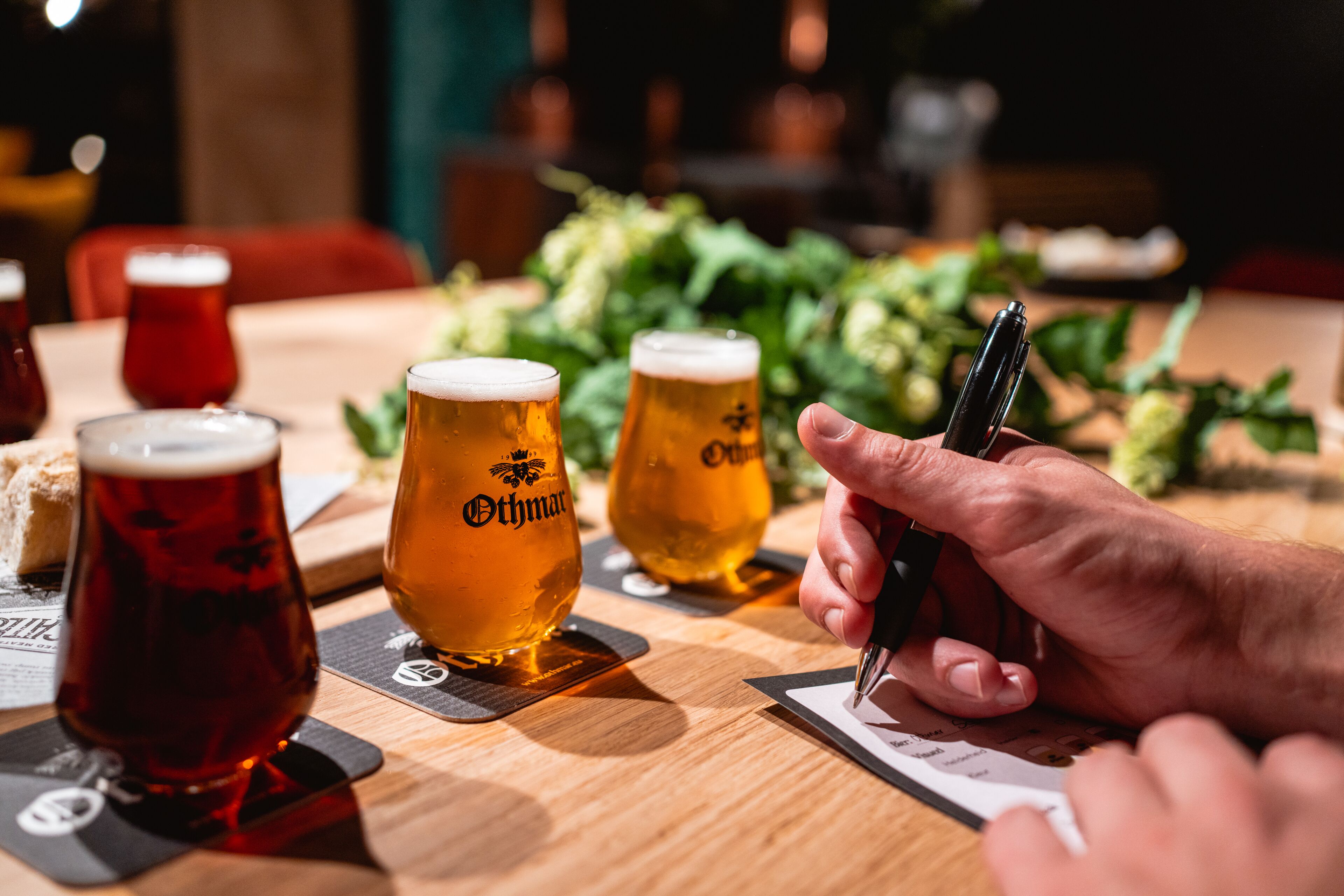 Een hand vasthoudt een pen, schrijven in een notitieboekje, met drie bierglazen ervoor.