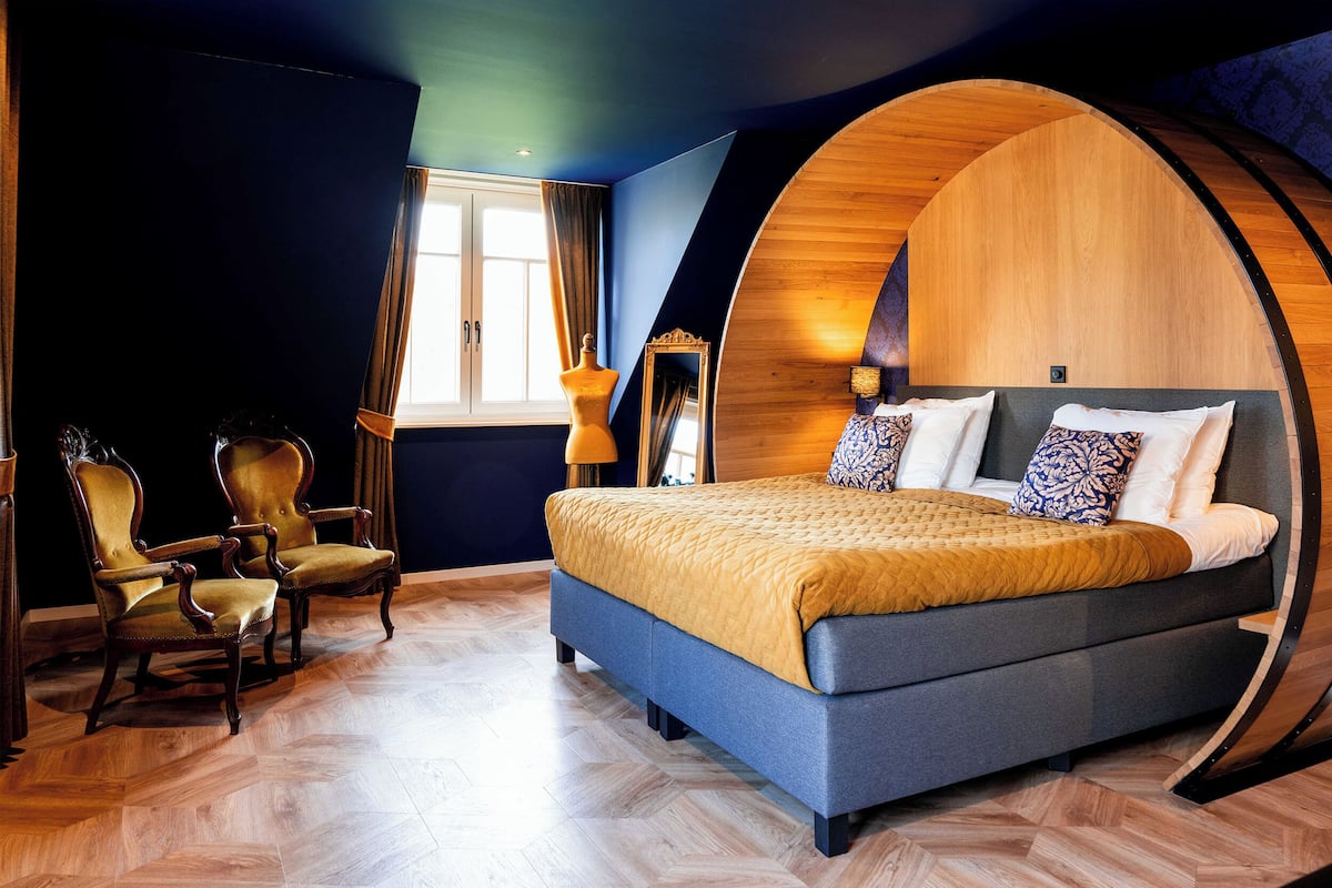 Une chambre à coucher avec un grand lit, deux fauteuils, un mur en arc de bois, une fenêtre avec des rideaux et un miroir.