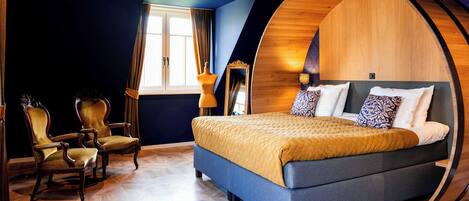 Un dormitorio con una cama grande, dos sillones, un arco de pared de madera, una ventana con cortinas y un espejo.