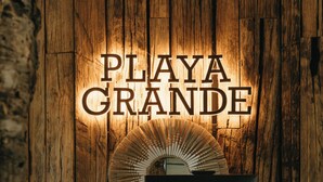 Un mur en bois sur lequel est apposée une enseigne lumineuse indiquant « PLAYA GRANDE ».