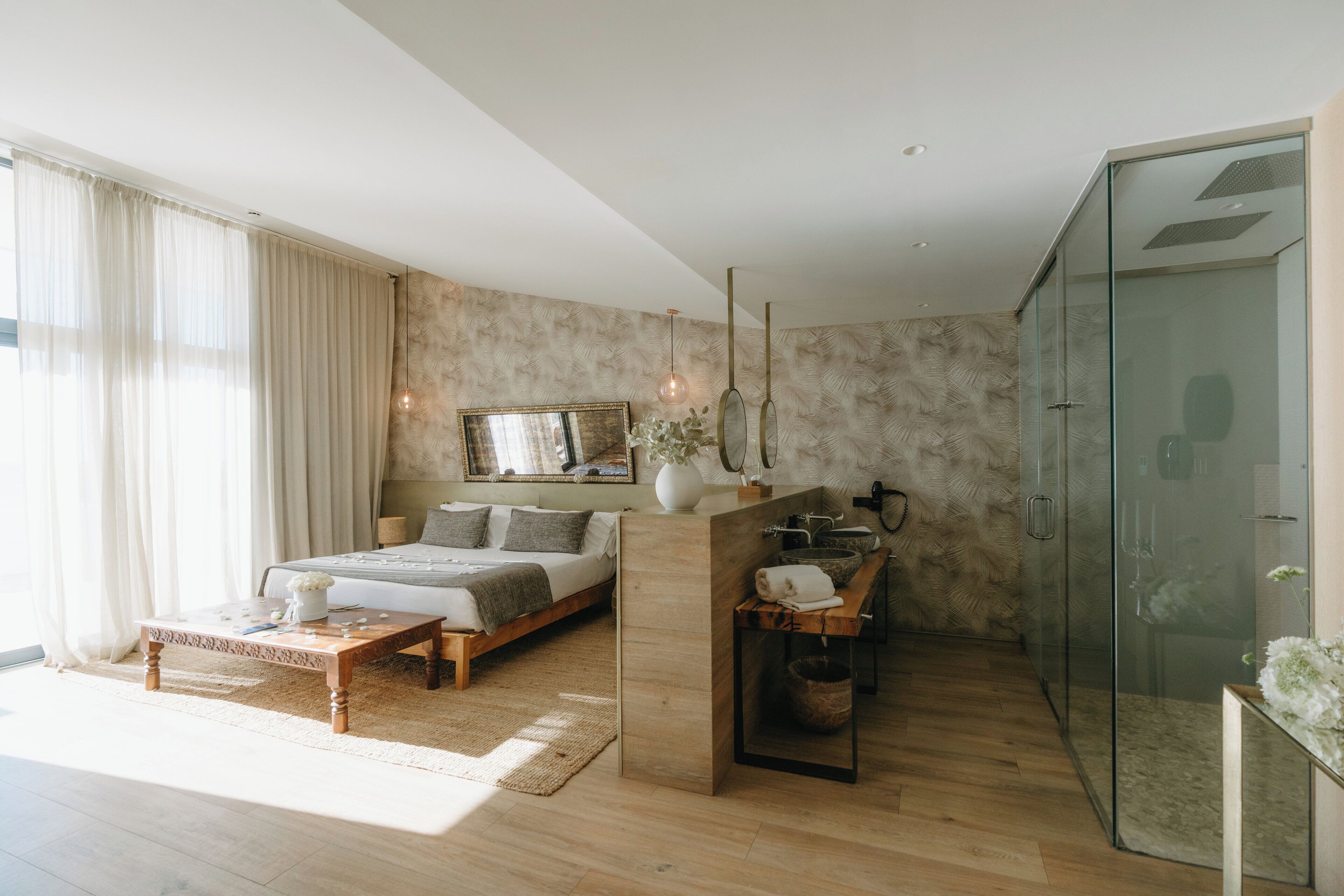 A modern bedroom with a bed, bedside table, and a glass shower enclosure.