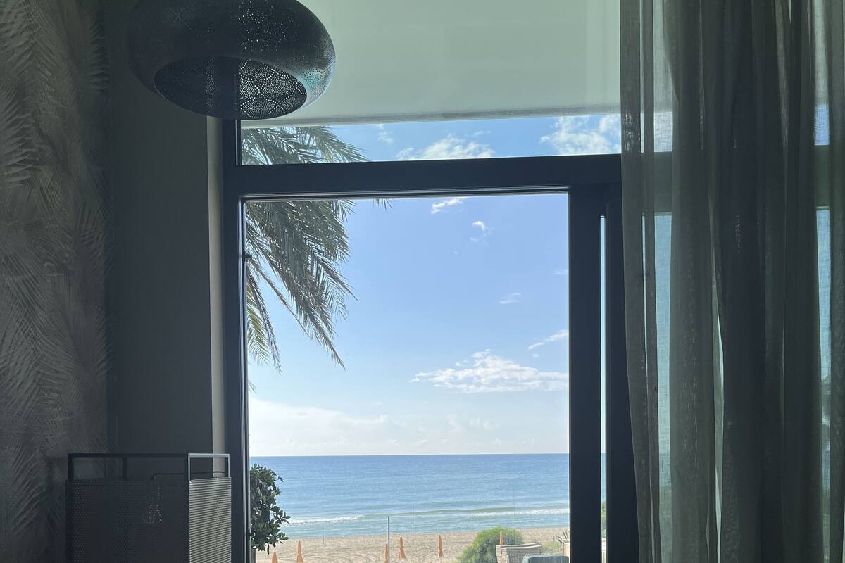 Een kamer met uitzicht op het strand, een groot raam, een bank en een plafondlamp.