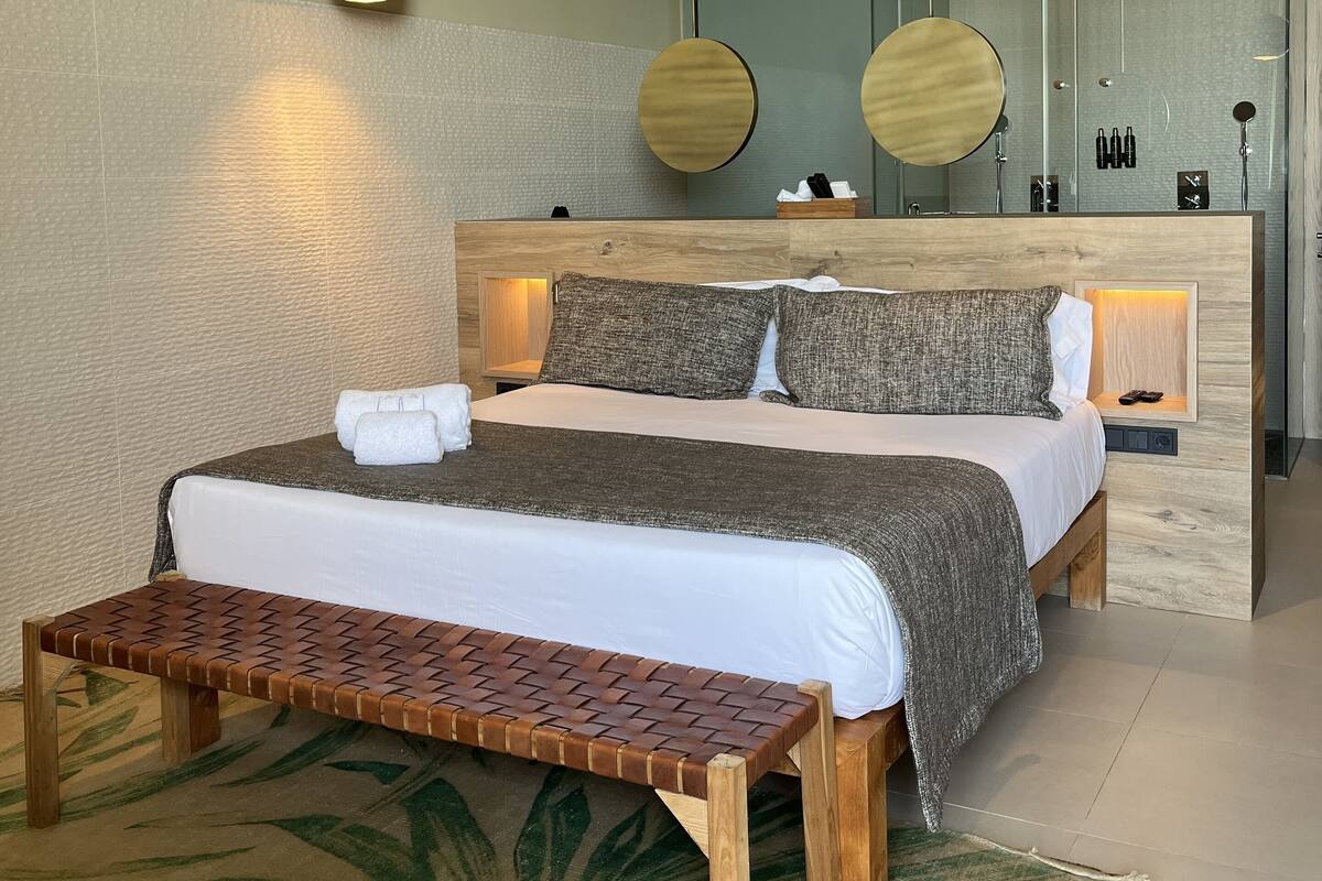 Een moderne slaapkamer met een houten plafond, een groot bed met een bankje, en een klein kitchenette.